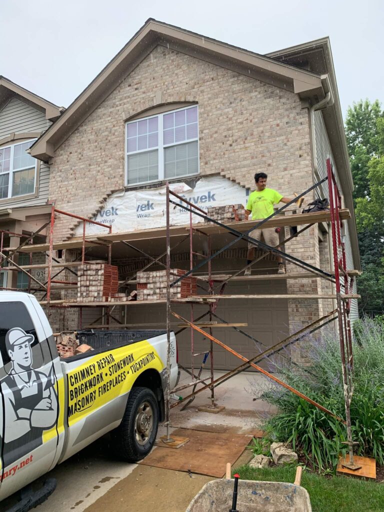 Adv Masonry worker performing brick restoration Naperville on residential garage wall with matching brick replacement